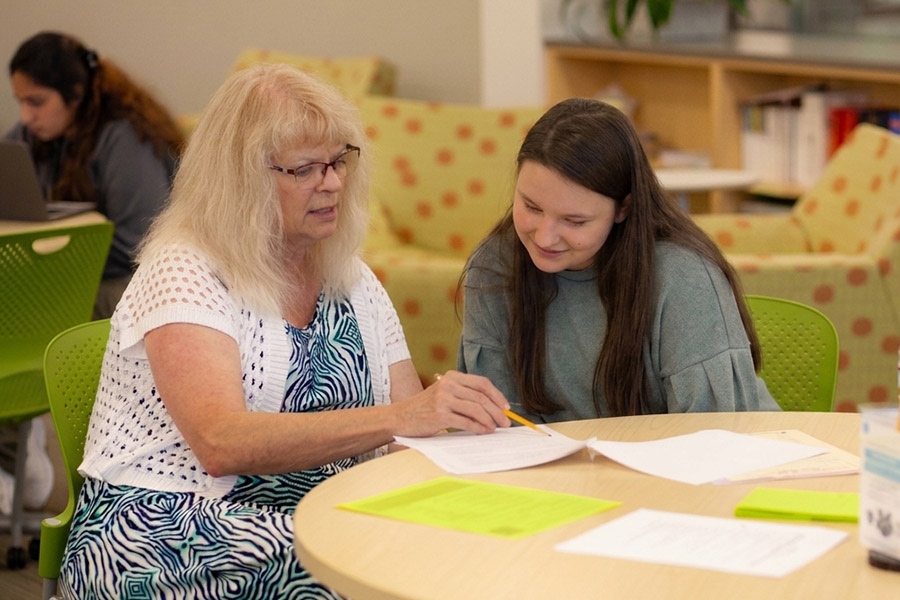 Faculty member reviewing paperwork with a student at a table in a campus lounge
