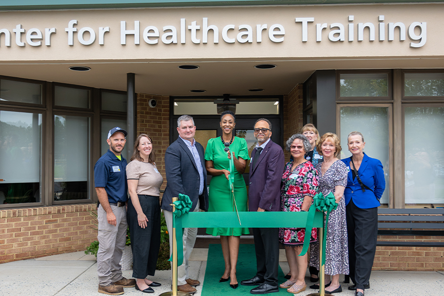 FCC leadership and staff pose for a ribbon-cutting outside the Miller Center for Healthcare Training, with a green ribbon and carpet leading to the entrance