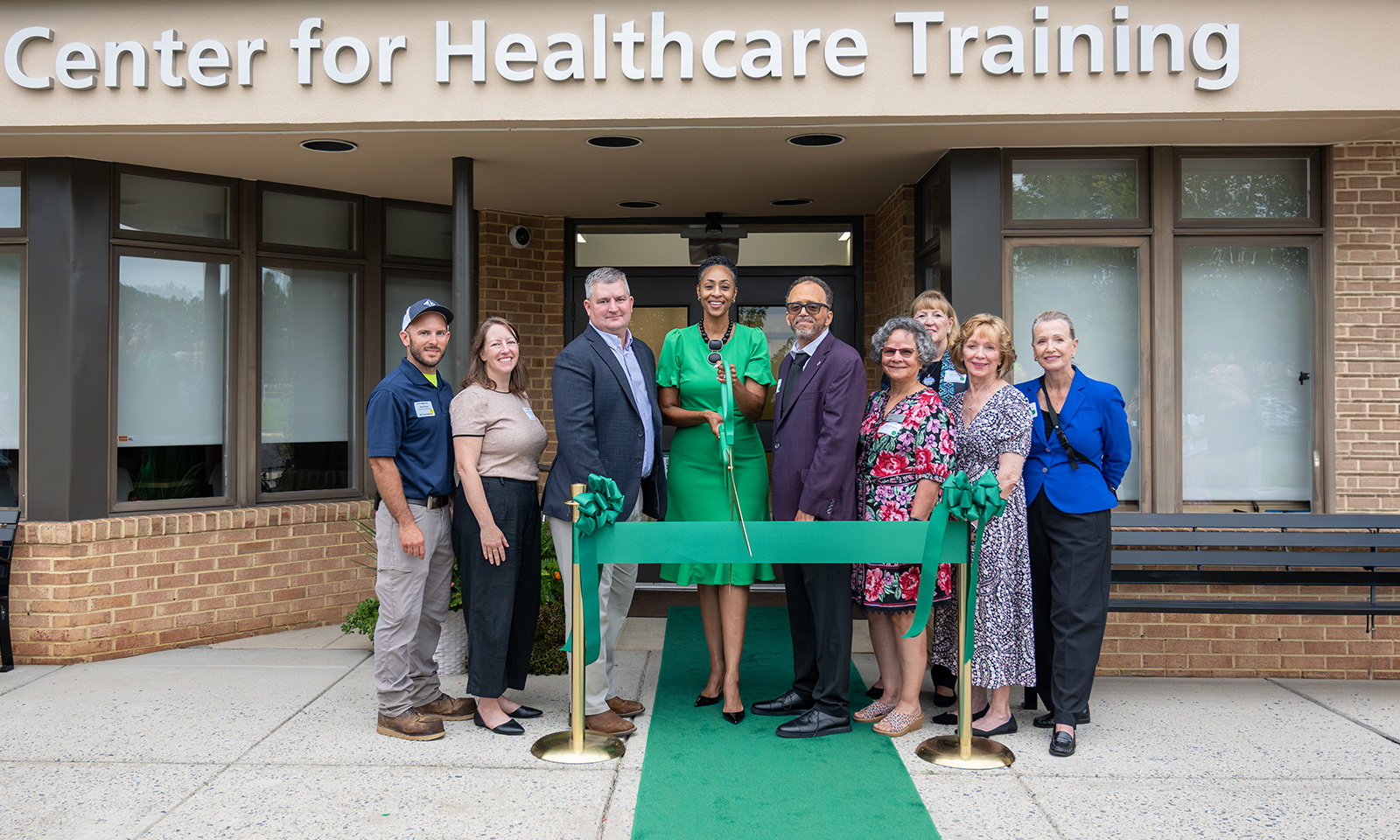 FCC leadership and staff pose for a ribbon-cutting outside the Miller Center for Healthcare Training, with a green ribbon and carpet leading to the entrance