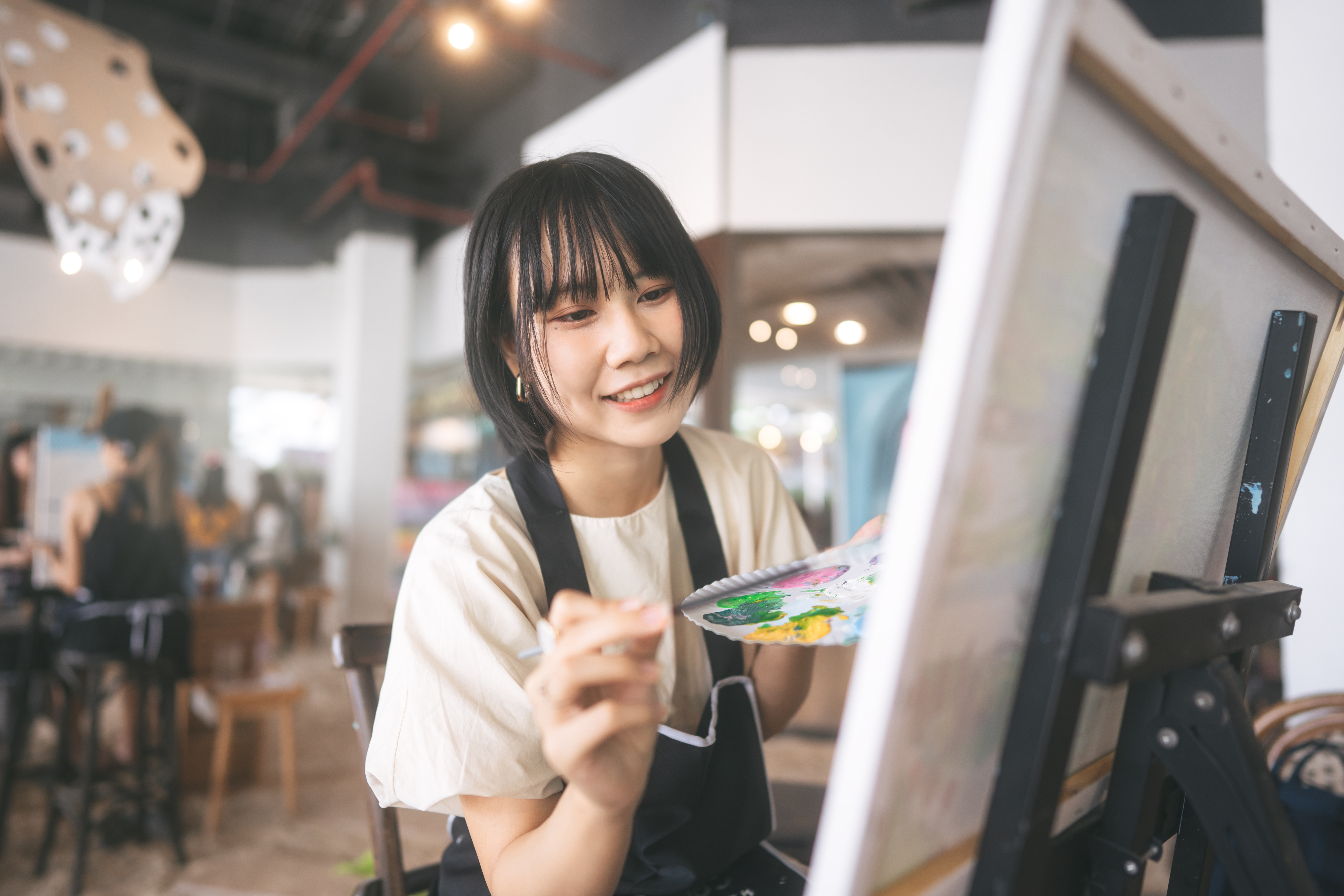 Young woman with a bob haircut joyfully painting on a canvas in a bright, artistic studio.